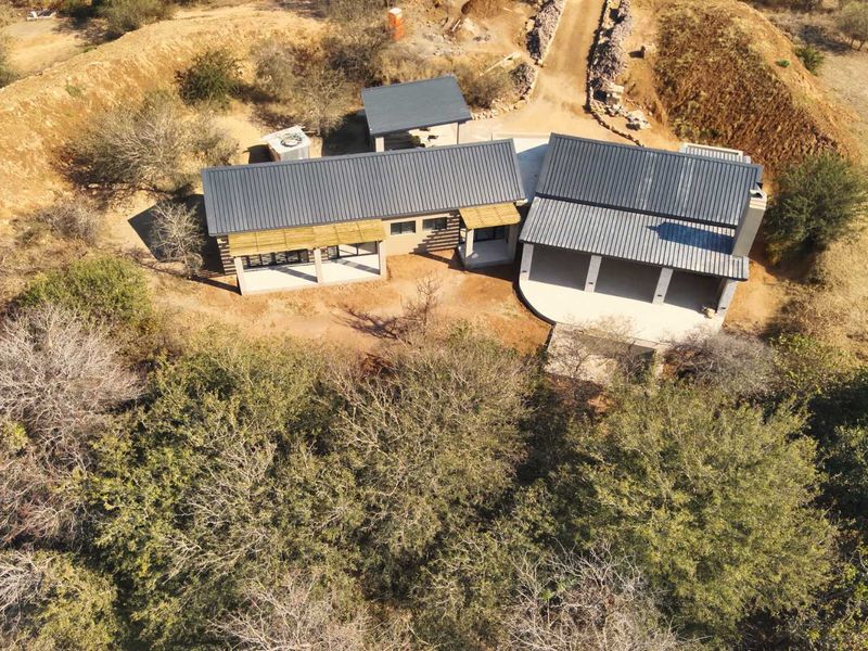 Aerial view of a modern house with metal roofing, covered patios, and timber pergola features, situated in a natural, undeveloped landscape setting.