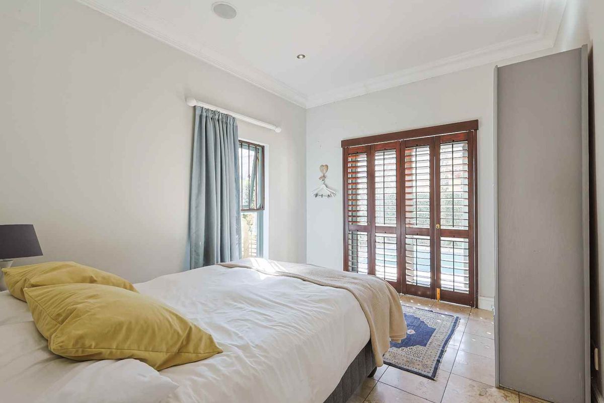 A bright bedroom featuring tiled flooring, built-in wardrobe storage, and wooden plantation shutters providing access to the exterior.