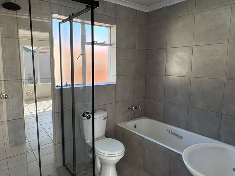 Modern bathroom featuring a walk-in shower with glass enclosure, a bathtub, pedestal basin, and toilet, finished with neutral grey wall and floor tiles.