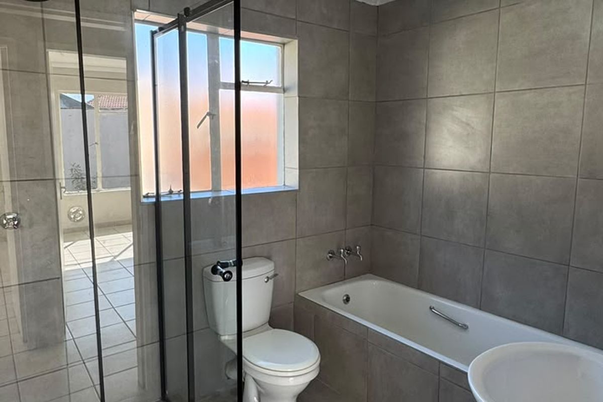 Modern bathroom featuring a walk-in shower with glass enclosure, a bathtub, pedestal basin, and toilet, finished with neutral grey wall and floor tiles.