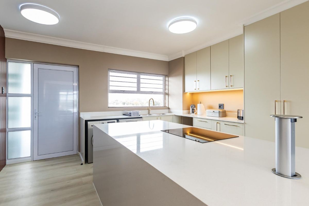 Modern kitchen featuring a large central island with integrated cooktop, sleek cabinetry, stone countertops, and under-cabinet lighting.