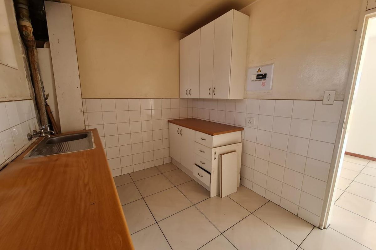 A compact kitchen area featuring tiled walls, wooden countertops, built-in cabinetry, and a stainless steel sink, requiring cosmetic updates.