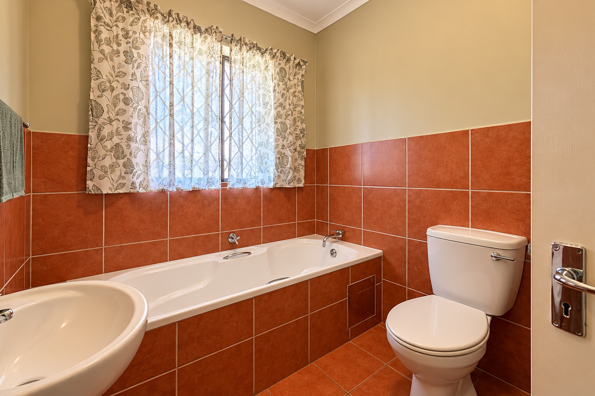 A functional bathroom featuring terracotta-toned wall and floor tiling, a built-in bathtub, a pedestal basin, and a standard close-coupled toilet.