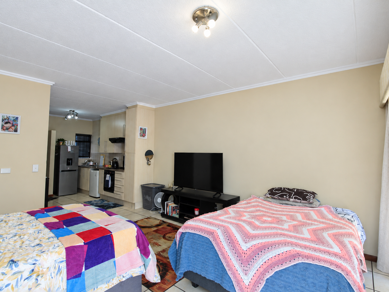 Open-plan living area featuring a compact kitchen with built-in cabinetry and appliances, seamlessly flowing into the bedroom space with tiled flooring throughout.