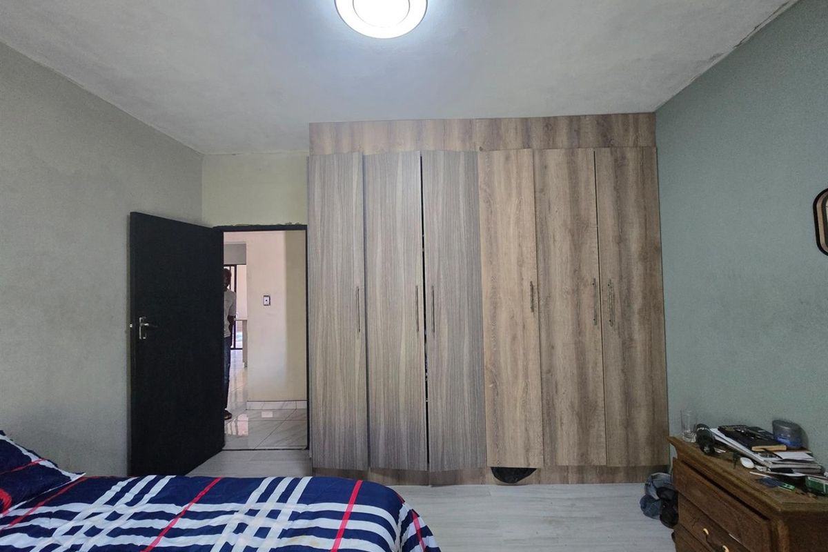 A bedroom featuring a large built-in wooden wardrobe and a central ceiling light fixture, with access to an adjacent hallway.