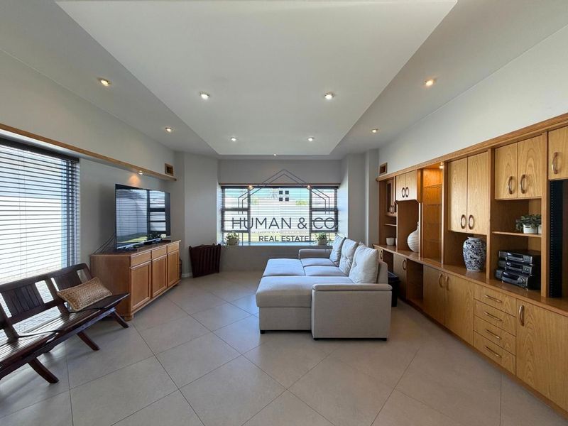 Spacious living room featuring neutral tiled flooring, recessed ceiling lights, and extensive built-in wooden cabinetry providing ample storage and display space.
