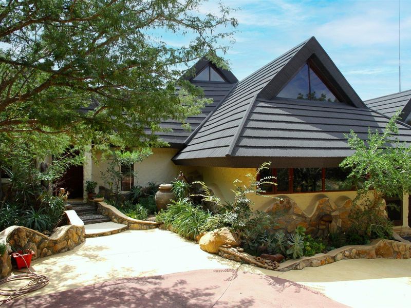 Front elevation of a unique architectural home featuring a multi-pitched tiled roof, stone-clad exterior walls, and distinctive triangular windows set within a landscaped garden.