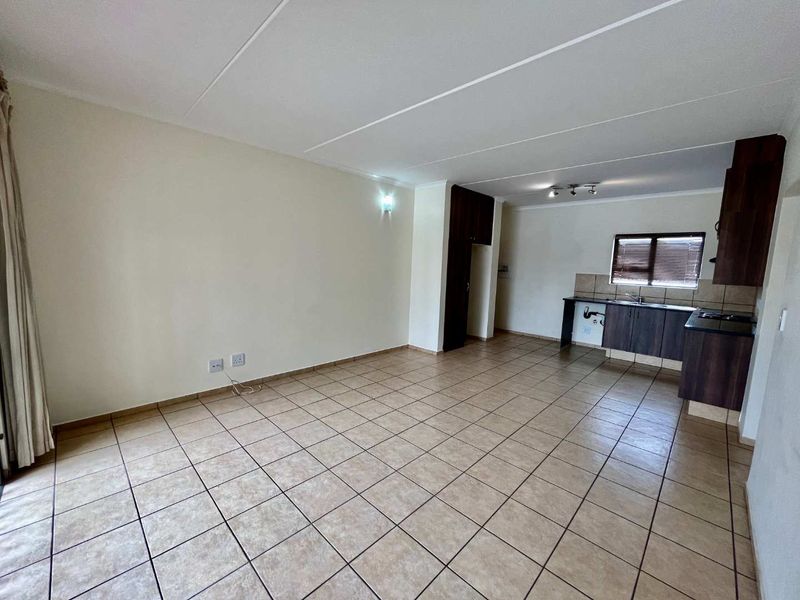 Spacious open-plan living area featuring tiled flooring and a functional kitchen with built-in cabinetry, sink, and hob.