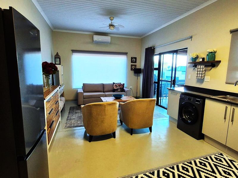 Open-plan living area featuring a compact kitchen with modern cabinetry, integrated sink, air conditioning, and sliding glass doors leading to an outdoor space.