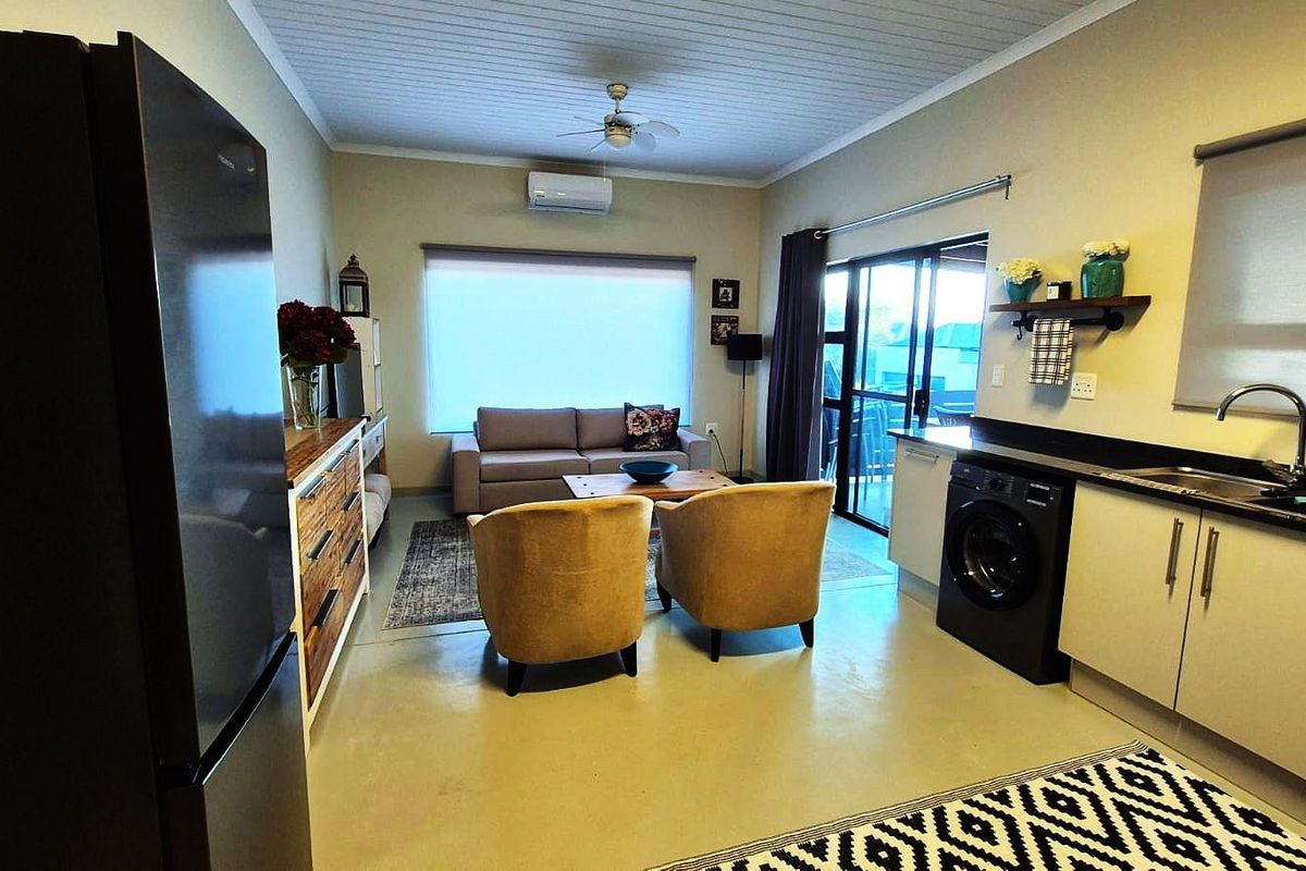 Open-plan living area featuring a compact kitchen with modern cabinetry, integrated sink, air conditioning, and sliding glass doors leading to an outdoor space.