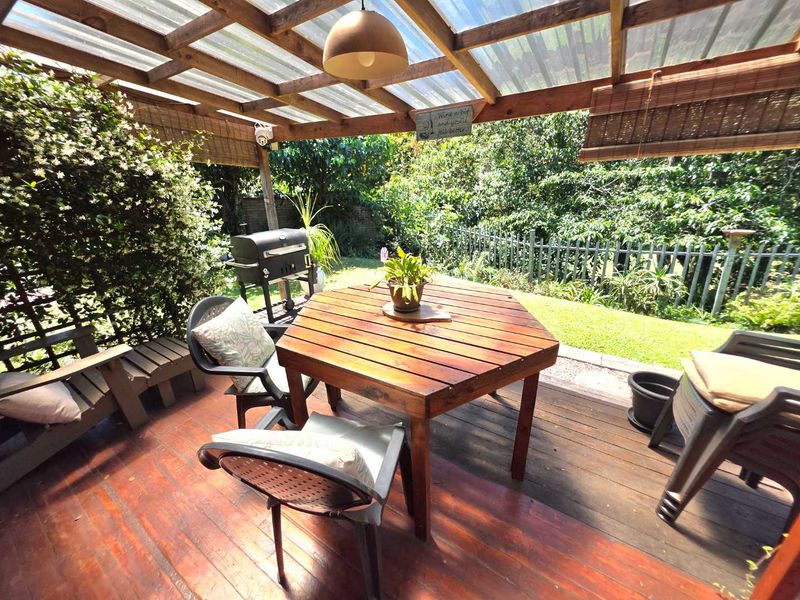 A covered outdoor patio featuring timber decking and a pergola structure, overlooking a private garden area.
