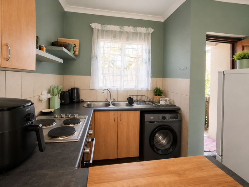 A functional kitchen featuring wood-finish cabinetry, dark countertops, a built-in electric hob, and a double sink with tiled splashbacks.