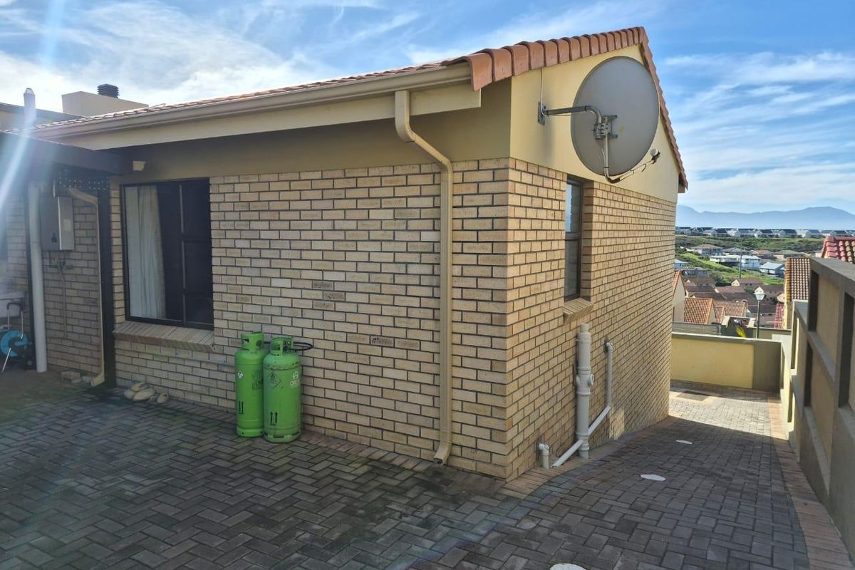 Rear exterior view of the property featuring face brick walls, tiled roofing, and a paved driveway area.