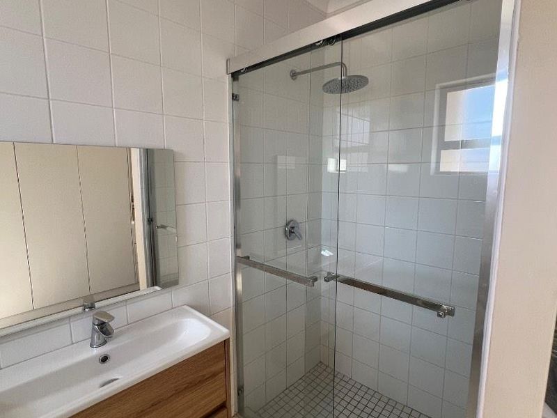 A modern bathroom featuring a glass-enclosed shower with a rain shower head, a wall-mounted vanity with an integrated basin, and neutral tiled finishes.