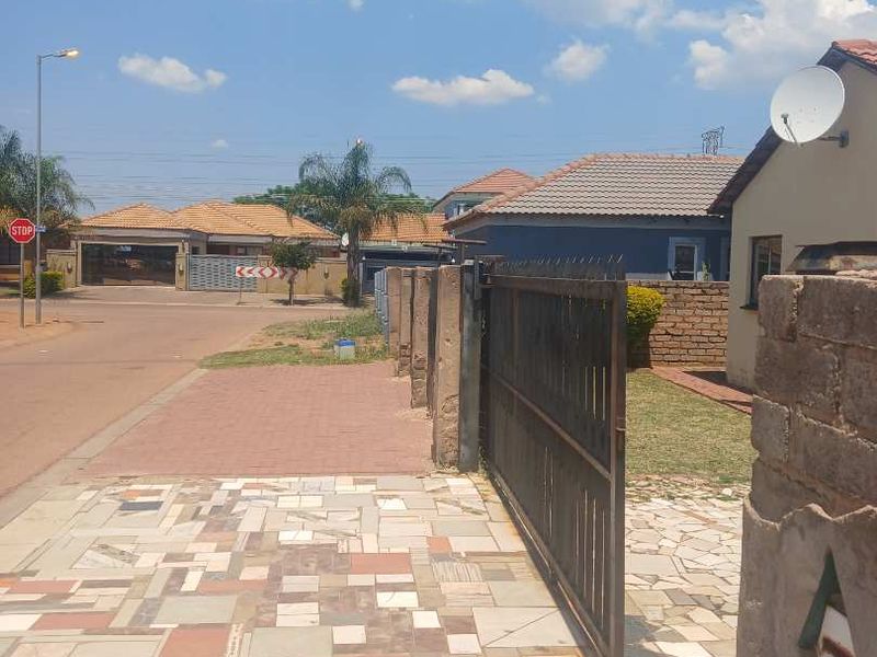Street view showing the property entrance with a paved driveway, metal sliding gate, and brick boundary wall in a residential neighbourhood.