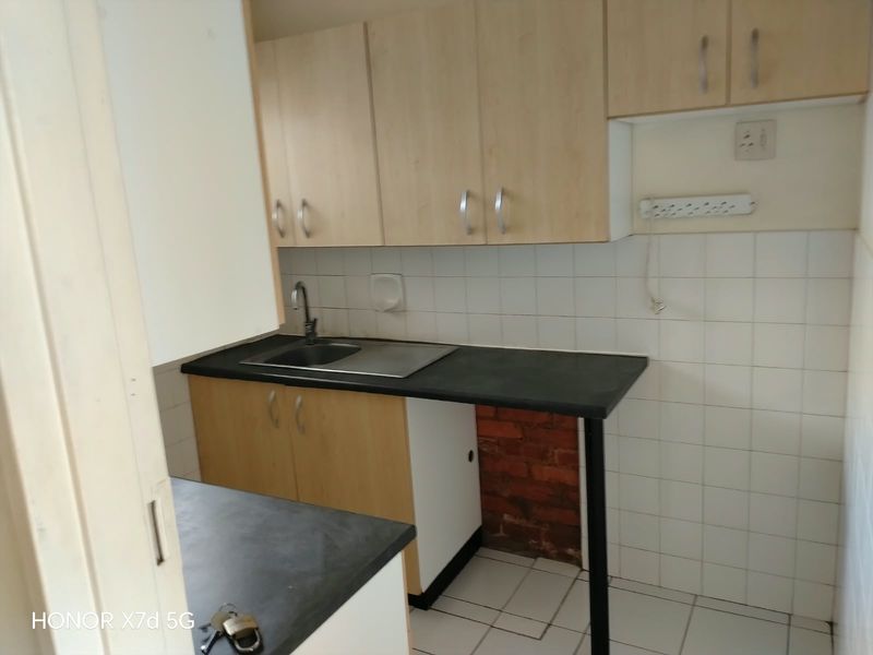 A compact kitchen area featuring laminate cabinetry, a stainless steel sink, tiled backsplash, and tiled flooring, currently requiring some finishing work.