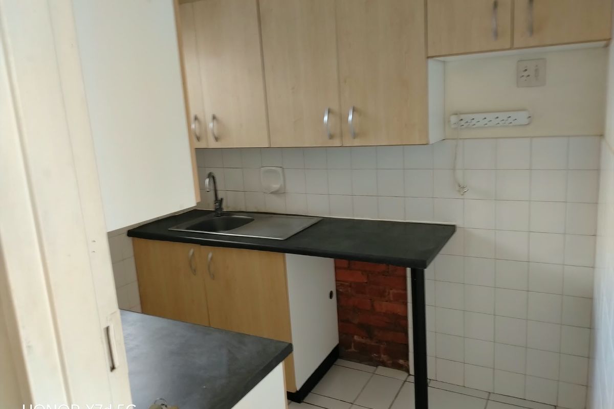 A compact kitchen area featuring laminate cabinetry, a stainless steel sink, tiled backsplash, and tiled flooring, currently requiring some finishing work.