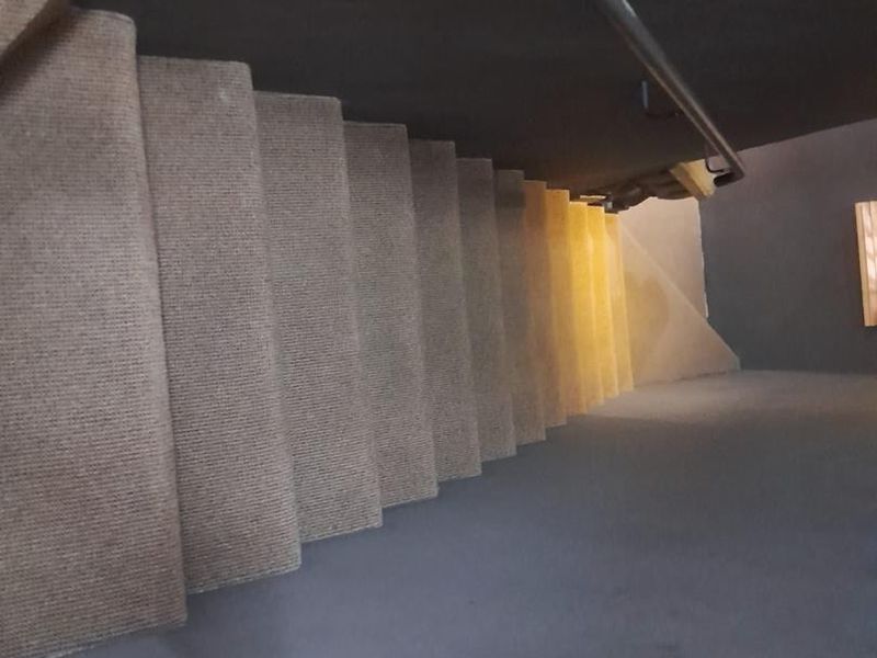 A view looking down a carpeted staircase featuring a dark-painted ceiling and a mounted metal handrail.
