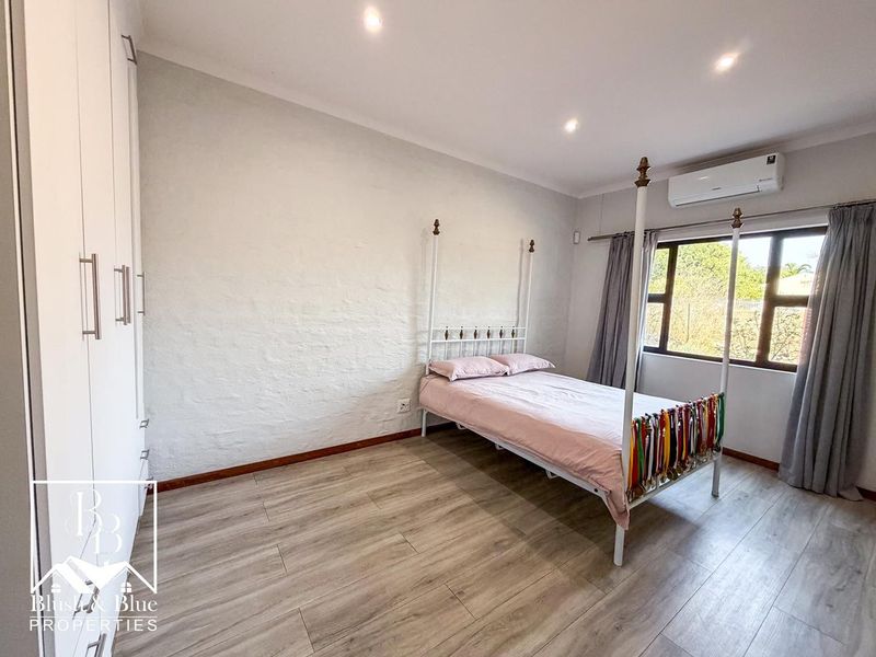 A well-maintained bedroom featuring light wood-look laminate flooring, built-in cupboards, recessed lighting, and a wall-mounted air conditioning unit.
