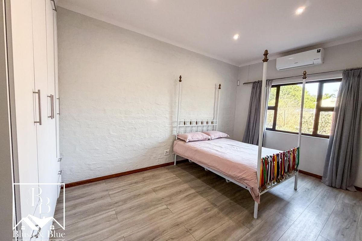 A well-maintained bedroom featuring light wood-look laminate flooring, built-in cupboards, recessed lighting, and a wall-mounted air conditioning unit.