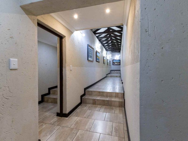 A long, tiled hallway featuring stepped floor levels, recessed lighting, and exposed timber ceiling beams, connecting different sections of the home.