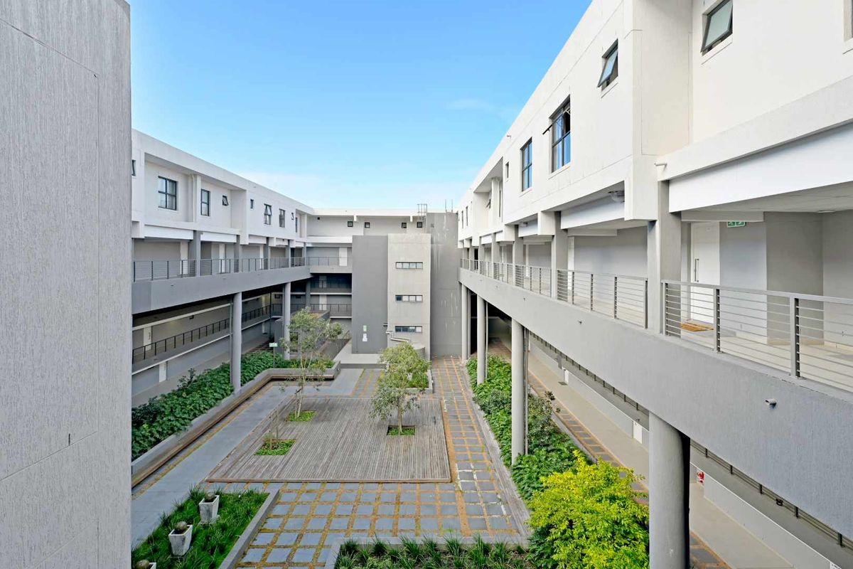 A modern apartment complex courtyard featuring a central landscaped area with wooden decking, paved pathways, and multi-level walkways with metal railings.