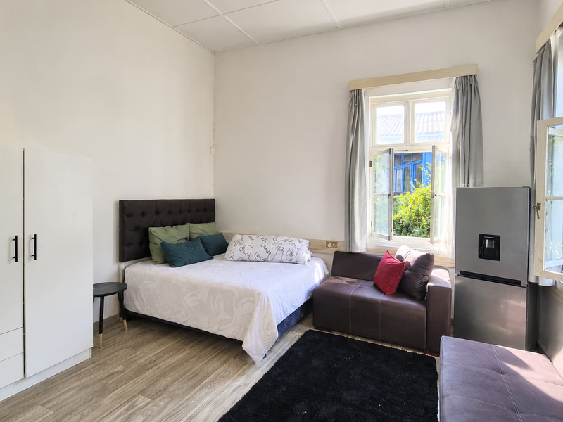 A bedroom featuring laminate flooring, a built-in wardrobe, and large casement windows providing natural light and garden views.