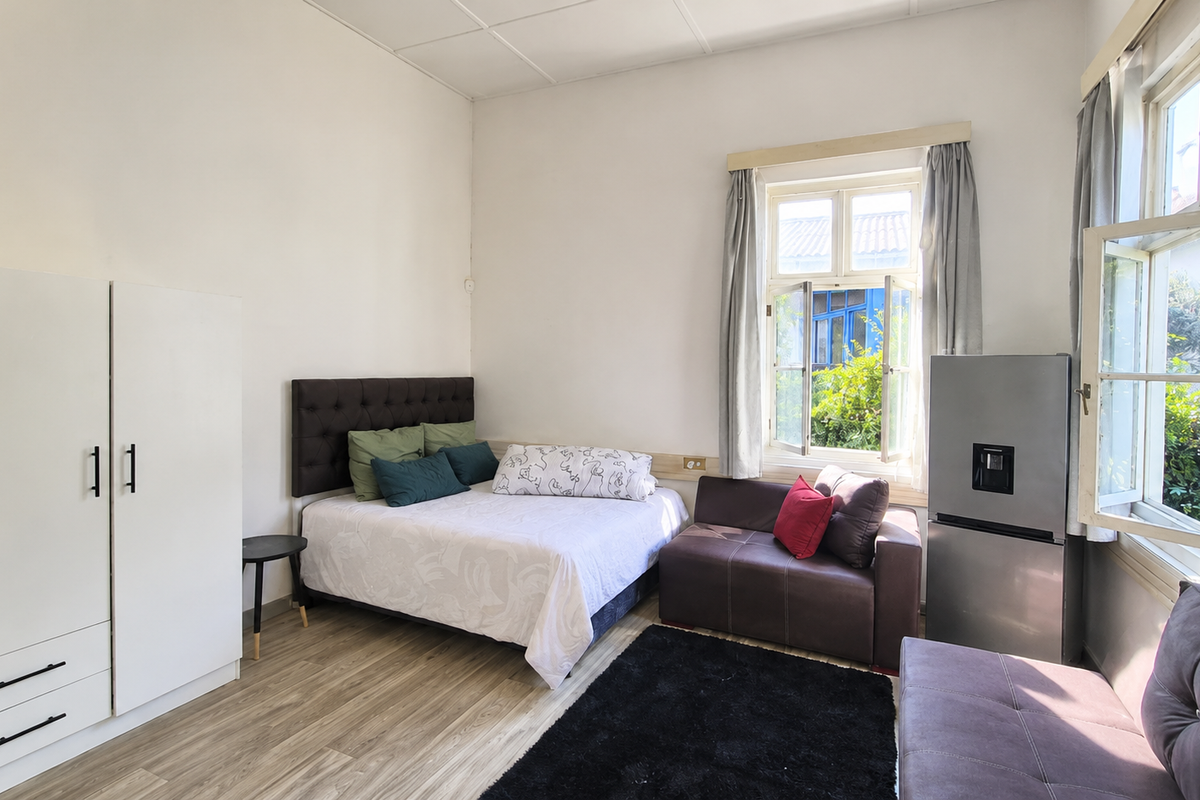 A bedroom featuring laminate flooring, a built-in wardrobe, and large casement windows providing natural light and garden views.
