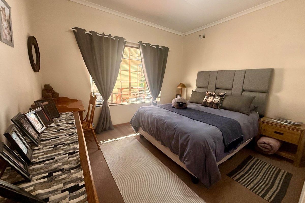 A well-lit bedroom featuring neutral walls, carpeted flooring, and a window with curtain treatments.