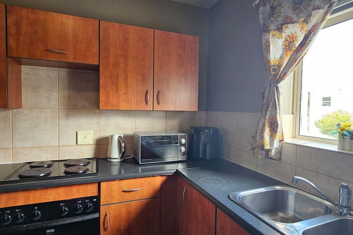 A functional kitchen featuring wood-look cabinetry, a dark laminate countertop, a built-in electric stove, and a stainless steel double sink.