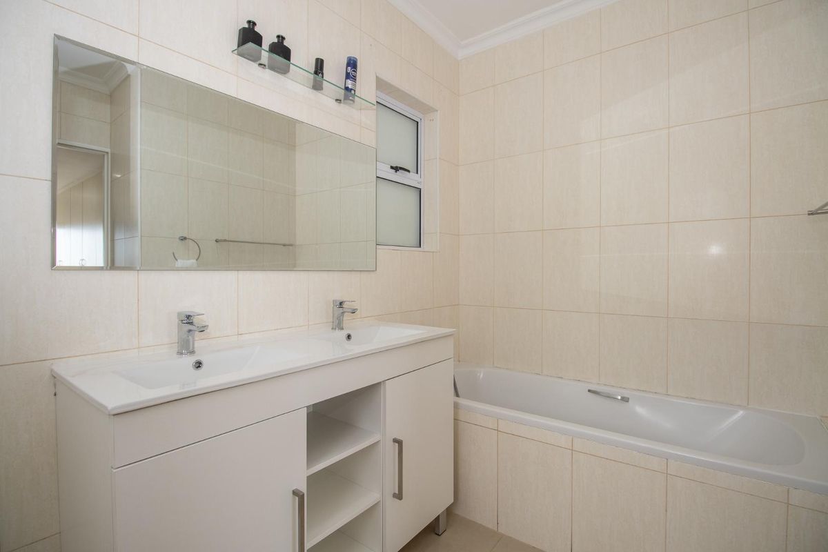 A clean, functional bathroom featuring a double vanity with white cabinetry, a large wall-mounted mirror, and a built-in bathtub with tiled surround.