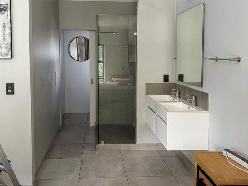 Modern bedroom featuring an en-suite bathroom with a floating double vanity, glass-enclosed shower, and ample built-in cupboard storage.