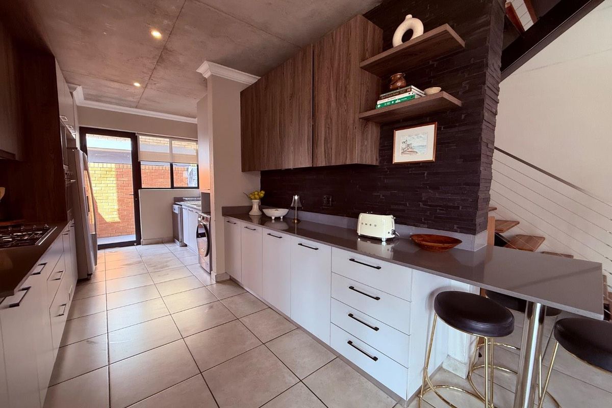 Modern kitchen featuring sleek cabinetry, stone countertops, a breakfast bar, and an exposed concrete ceiling, seamlessly flowing into the adjacent living area.