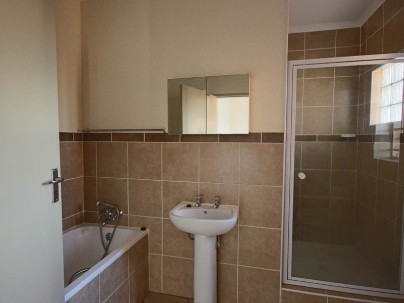 A functional bathroom featuring a pedestal basin, a built-in bathtub, and a separate shower enclosure with neutral wall tiling.