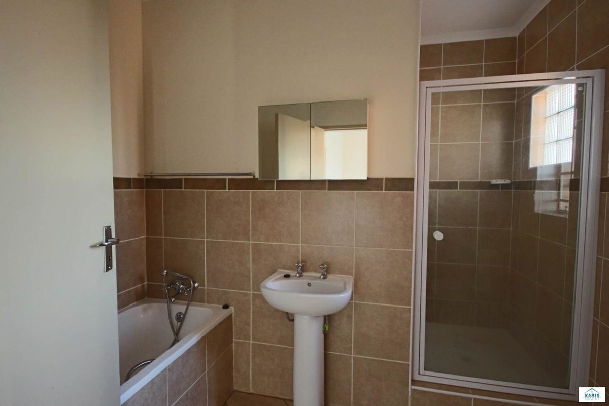 A functional bathroom featuring a pedestal basin, a built-in bathtub, and a separate shower enclosure with neutral wall tiling.