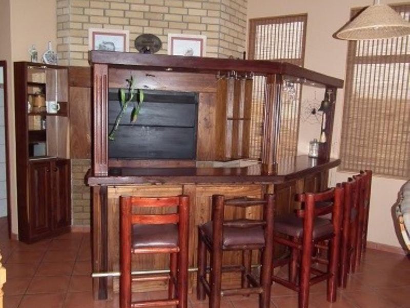 A rustic indoor bar area featuring a built-in timber counter, brick fireplace, exposed ceiling beams, and tiled flooring.