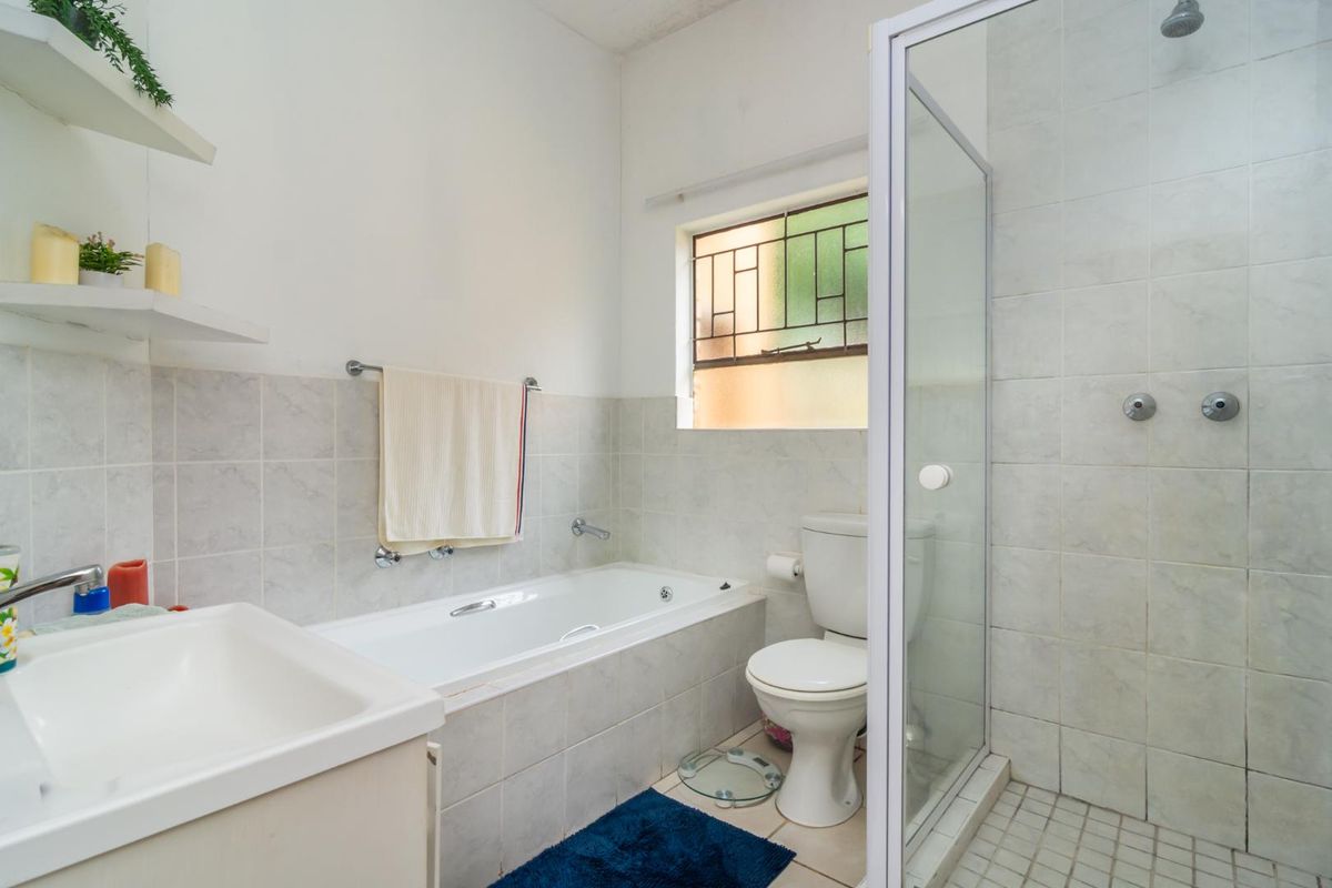 A functional bathroom featuring a built-in bathtub, a separate glass-enclosed shower, a toilet, and a vanity basin with tiled walls.