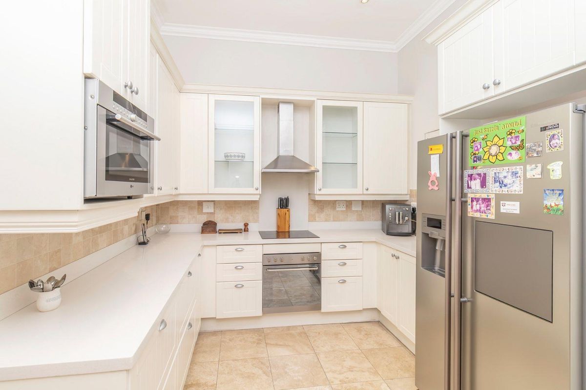 A well-maintained kitchen featuring cream cabinetry, stone countertops, a built-in oven, electric hob, stainless steel extractor fan, and tiled flooring.