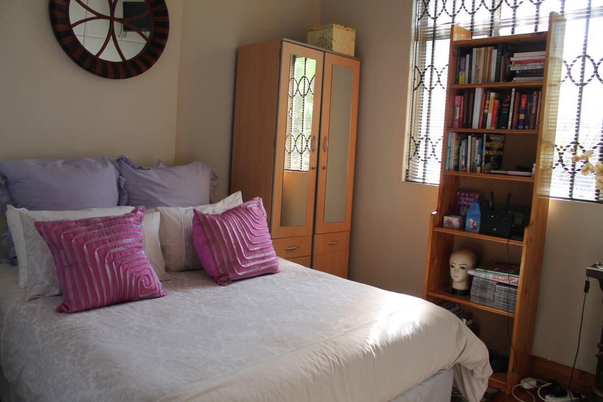 A functional bedroom featuring a built-in wardrobe and security bars on the window, providing a practical and secure living space.