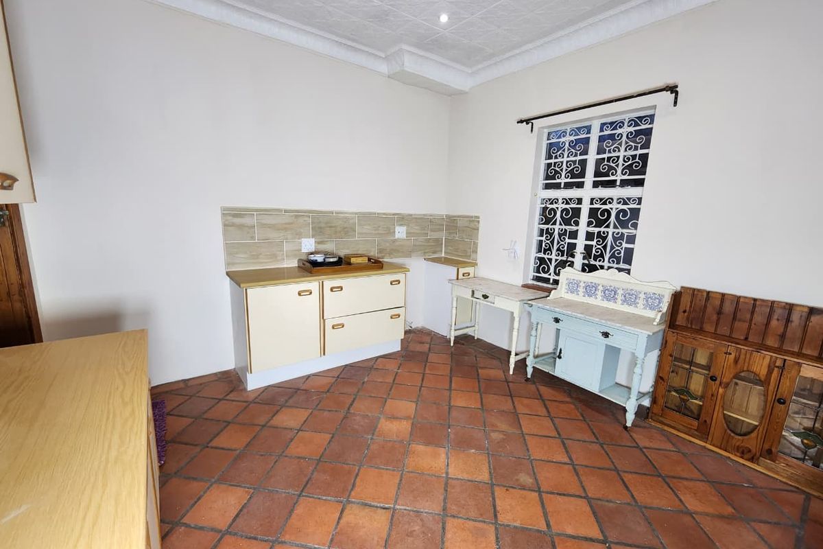 A functional kitchen area featuring terracotta floor tiles, a tiled splashback, and built-in base cabinetry with a window providing natural light.
