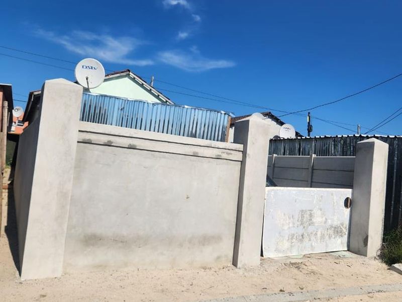 Front view of the property featuring a concrete boundary wall, gate pillars, and a metal entrance gate.