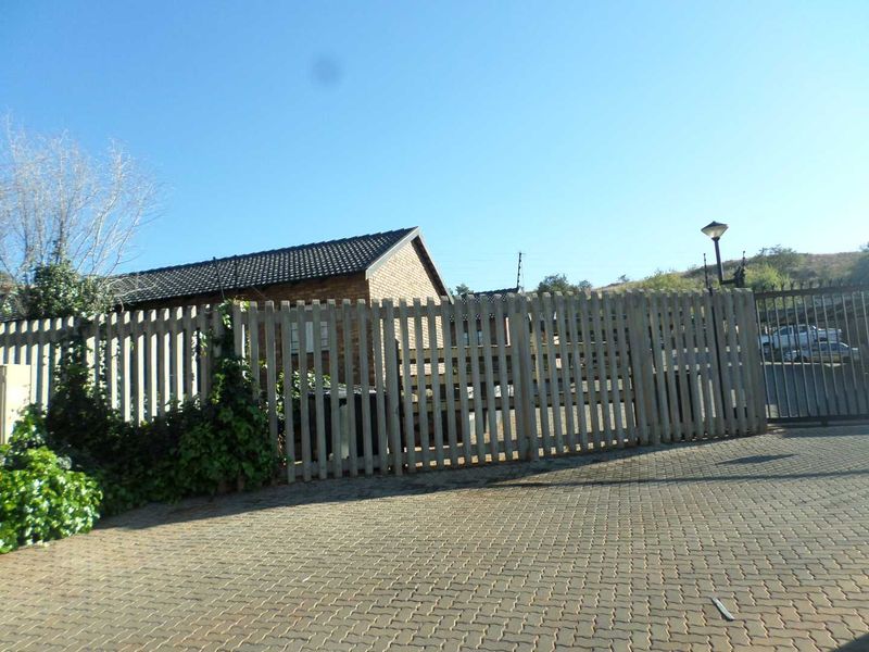 Front exterior view of the property featuring a paved driveway, timber fencing, and a brick building structure with a tiled roof.