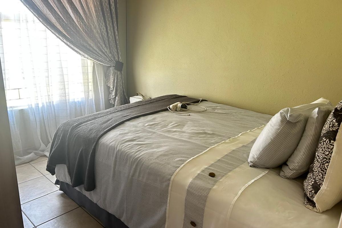 A functional bedroom featuring tiled flooring and natural light from a window with installed curtain hardware.
