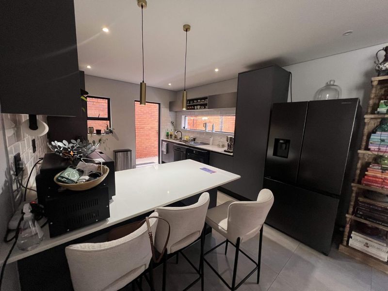 Modern kitchen featuring dark cabinetry, a central island with quartz countertops, sleek pendant lighting, and a tiled backsplash with direct access to the exterior.