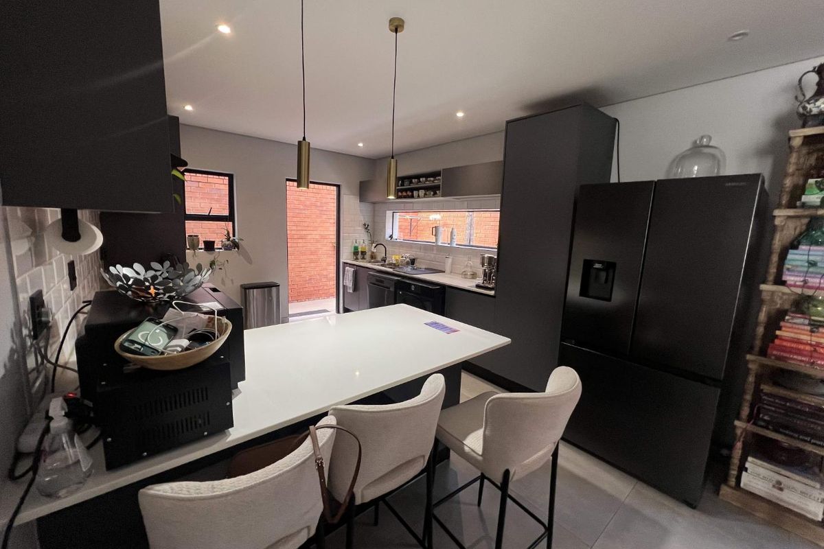 Modern kitchen featuring dark cabinetry, a central island with quartz countertops, sleek pendant lighting, and a tiled backsplash with direct access to the exterior.