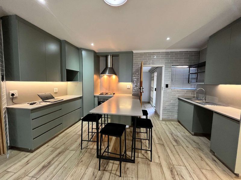 Modern kitchen featuring sage green cabinetry, stone countertops, integrated appliances, subway tile backsplash, and wood-look tiled flooring with a central breakfast island.