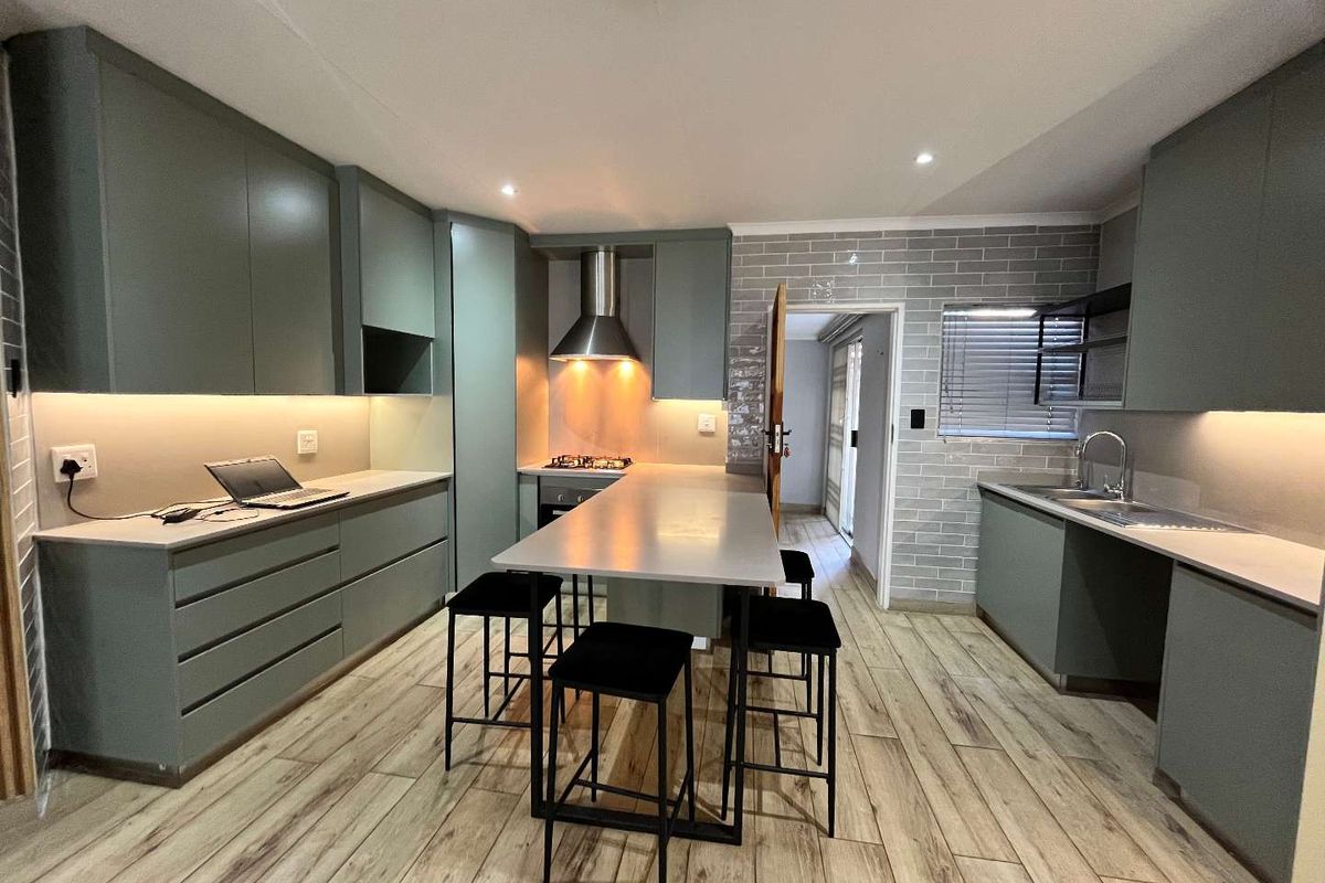 Modern kitchen featuring sage green cabinetry, stone countertops, integrated appliances, subway tile backsplash, and wood-look tiled flooring with a central breakfast island.
