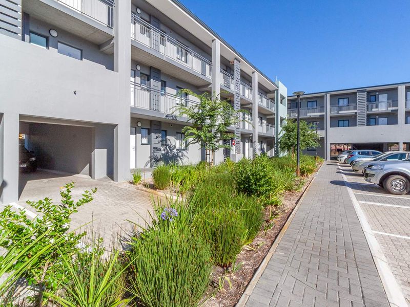 Exterior view of a modern apartment complex featuring paved parking areas, landscaped garden beds, and private balconies for each unit.