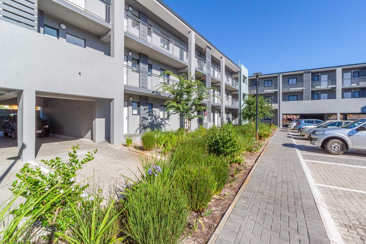 Exterior view of a modern apartment complex featuring paved parking areas, landscaped garden beds, and private balconies for each unit.