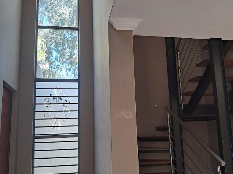 Entrance hall featuring a double-volume ceiling, a tall window providing natural light, a decorative chandelier, and an open-tread staircase with a metal balustrade.